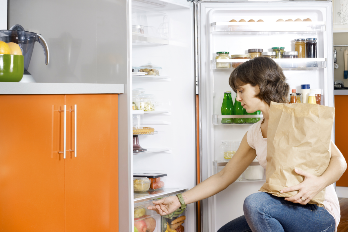 a woman putting away groceries in an energy efficient refrigerator.