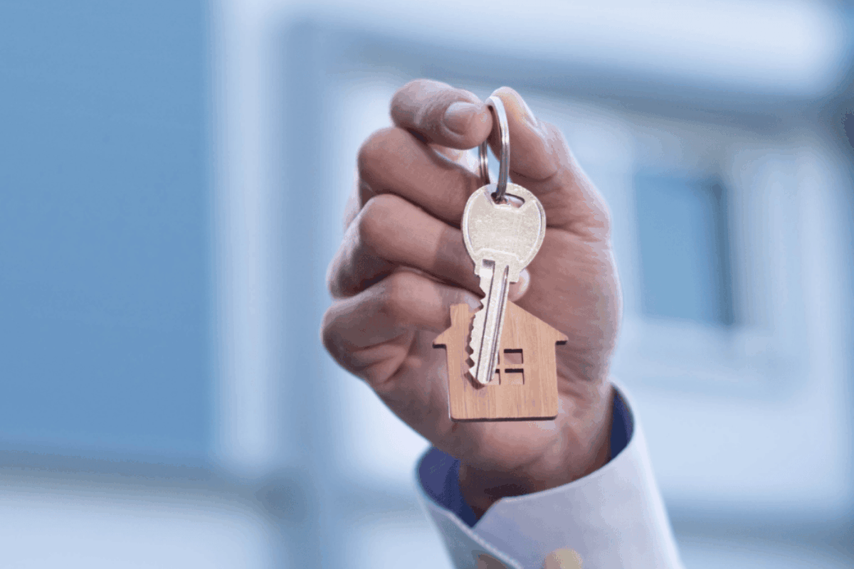 a hand holding up a pair of keys to a rented home with a keychain of a wooden house.