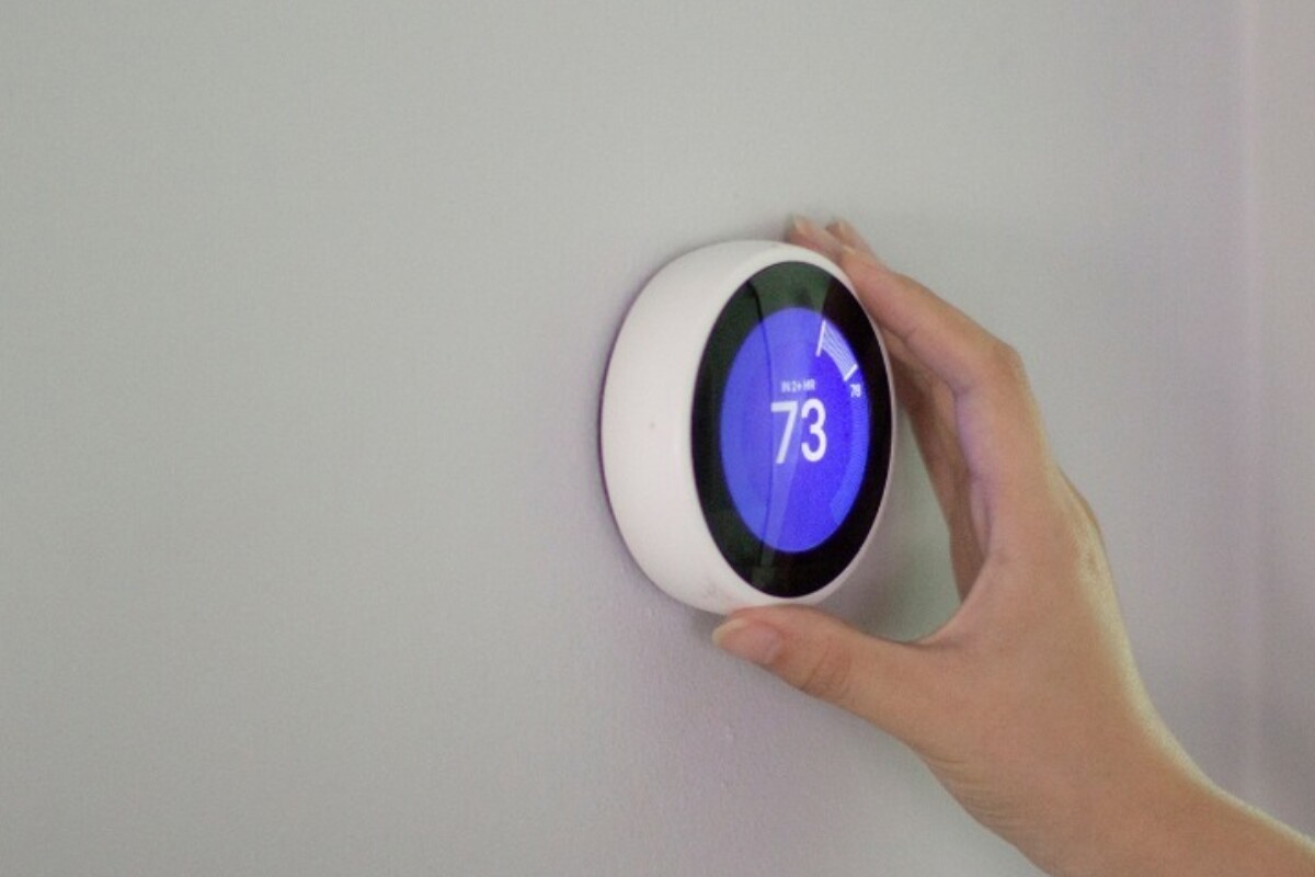 a person adjusting a smart thermostat to set it to 73 degrees Fahrenheit in their home.