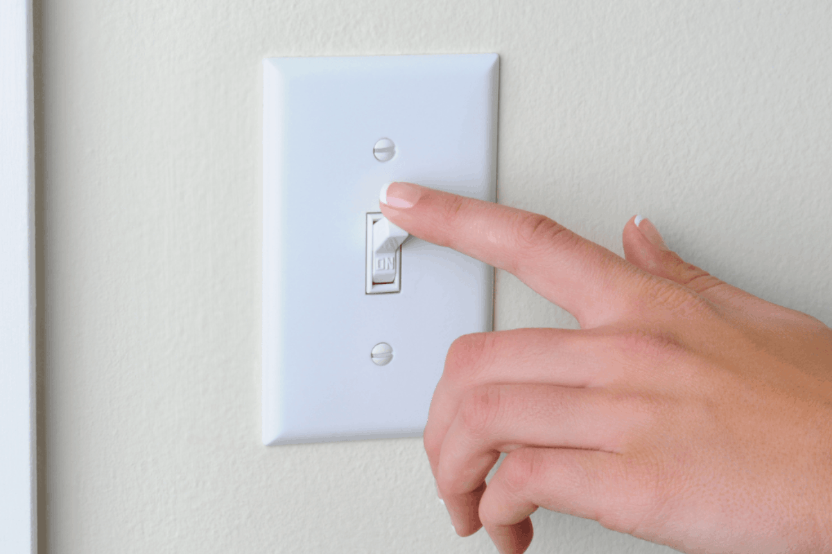 a hand turning a light switch off to help conserve energy in their home.