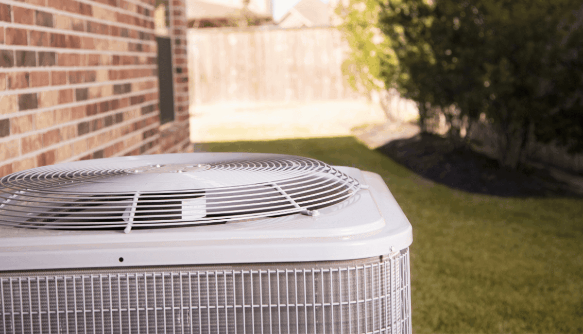 An outdoor air conditioner unit on a lawn next to a house