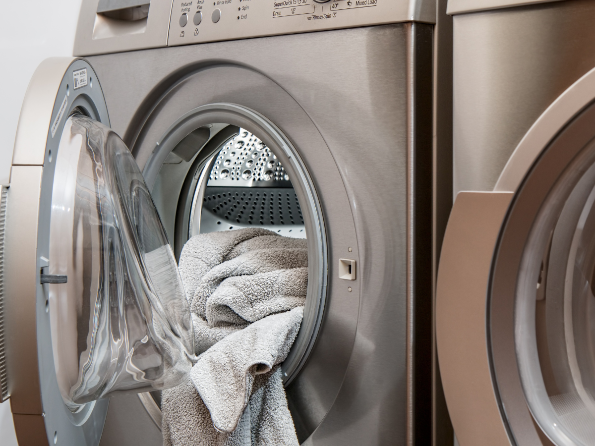 an electric clothes dryer with towels coming out of its door. Running laundry machines energy efficiently can help save money.