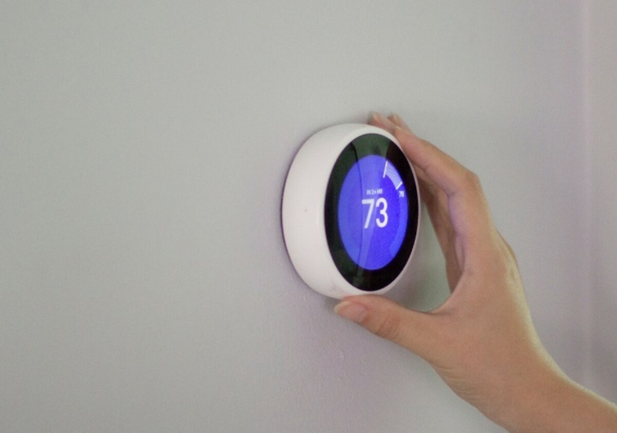 a person adjusting a smart thermostat to set it to 73 degrees Fahrenheit in their home.