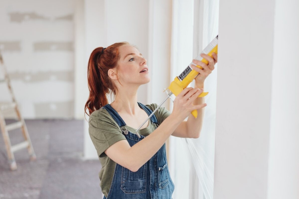 Woman sealing edges of a window with a caulk gun