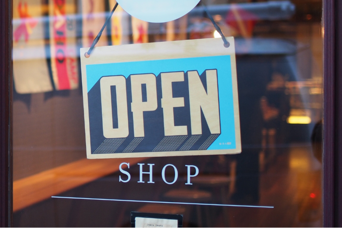 a sign on a glass entry door for a retail shop that is flipped to say, "Open".