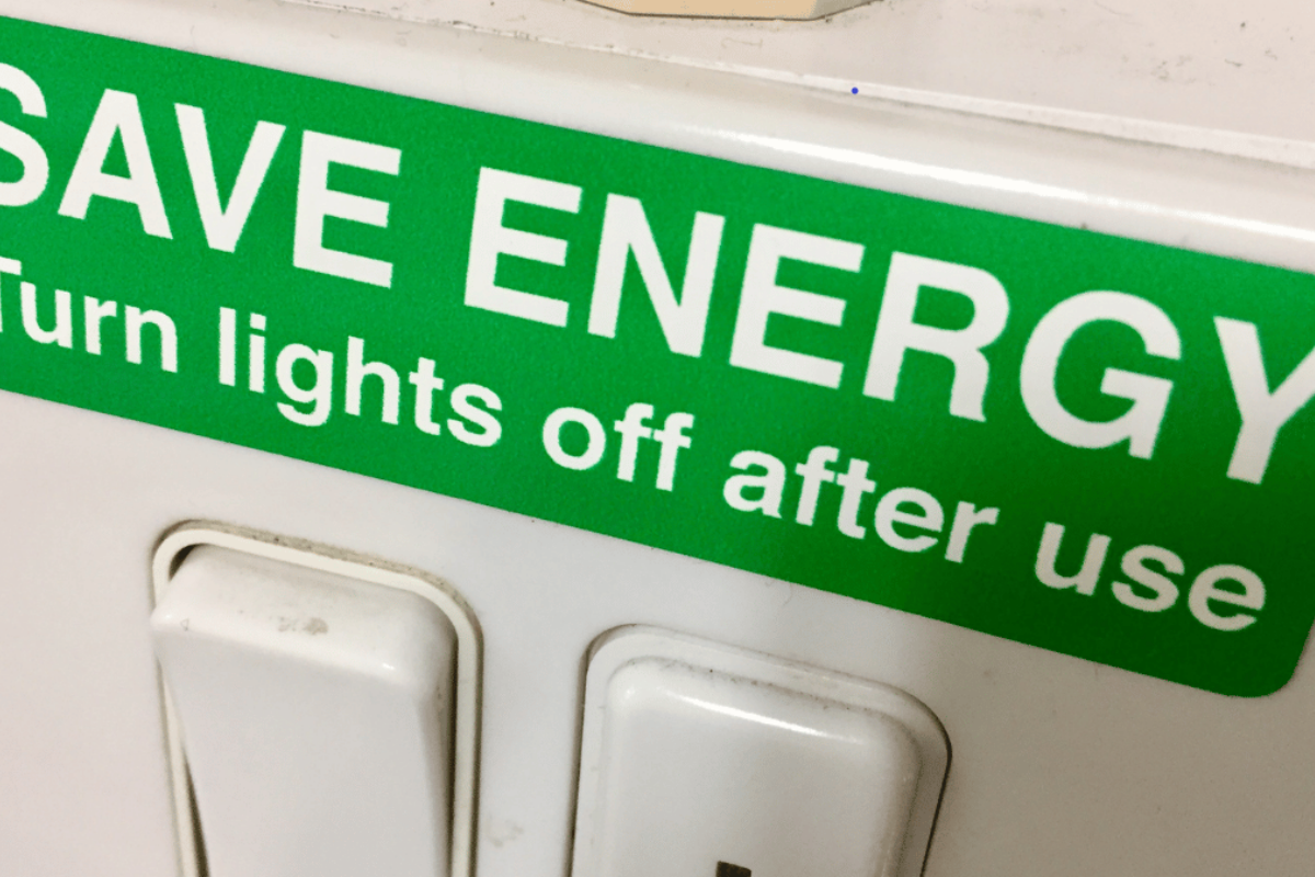 A label placed above a light switch inside a business that states save energy turn lights off after use