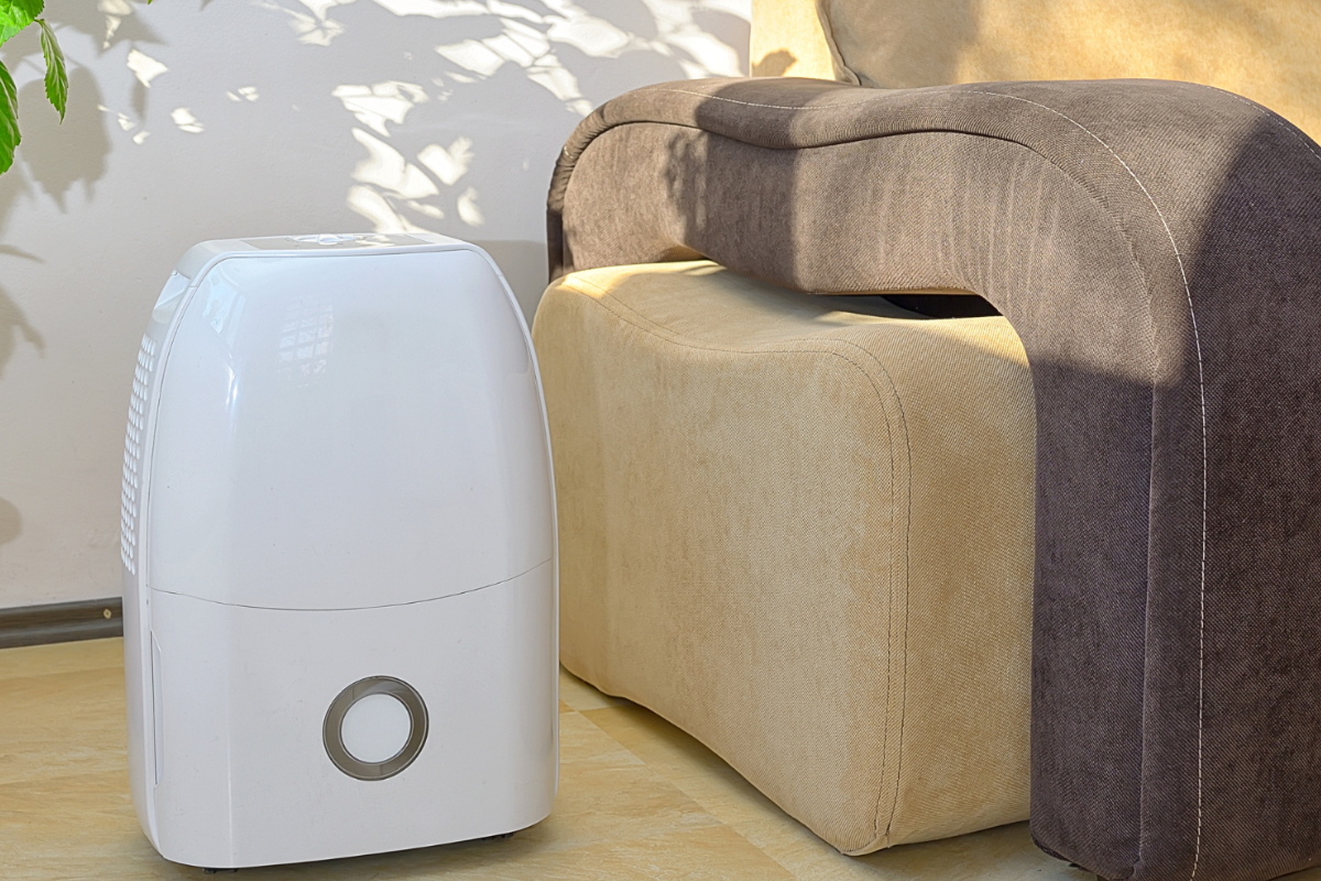 a dehumidifier on the ground next to a brown and beige couch.