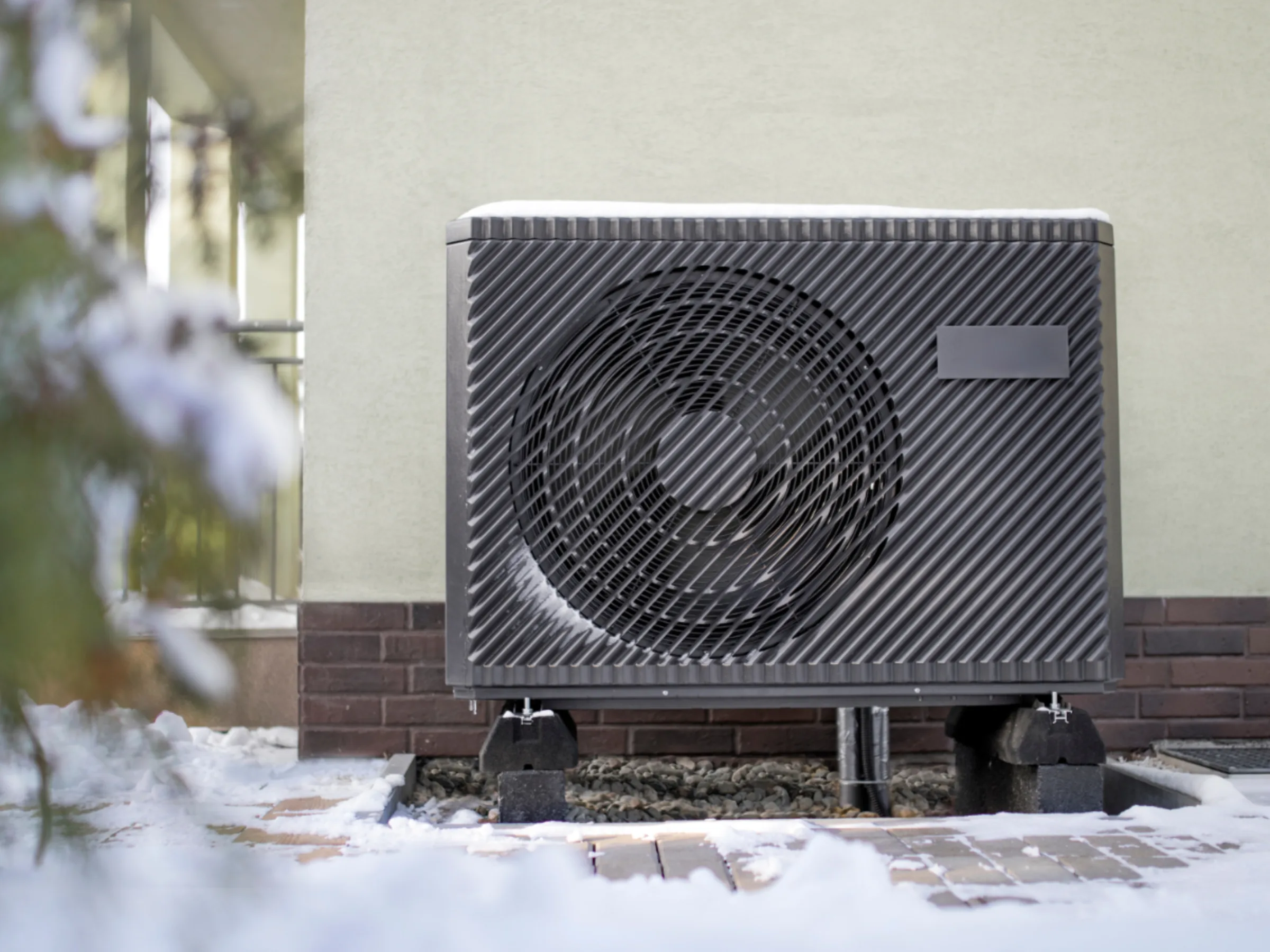 a cold climate air source heat pump outside of a home in the wintertime with snow on the ground.