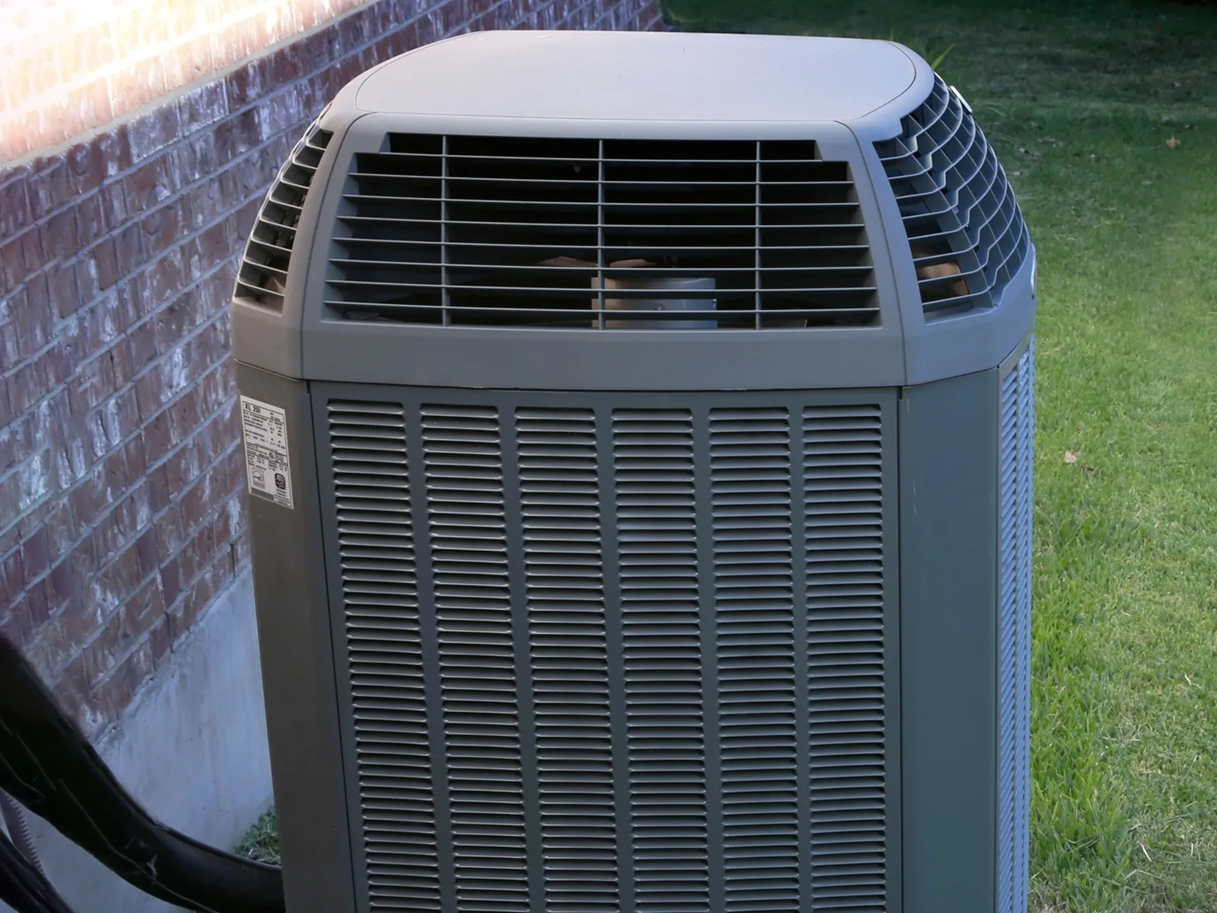 the top half of a central air conditioner attached to the outside of a house.