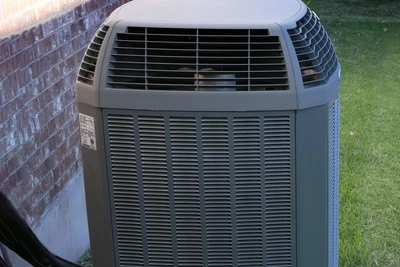 the top half of a central air conditioner attached to the outside of a house.