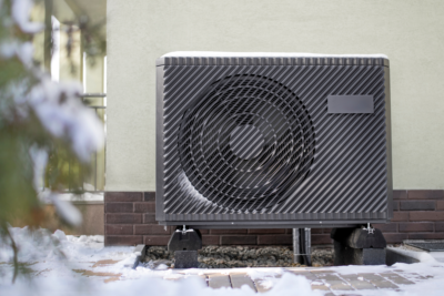 a cold climate air source heat pump outside of a home in the wintertime with snow on the ground.